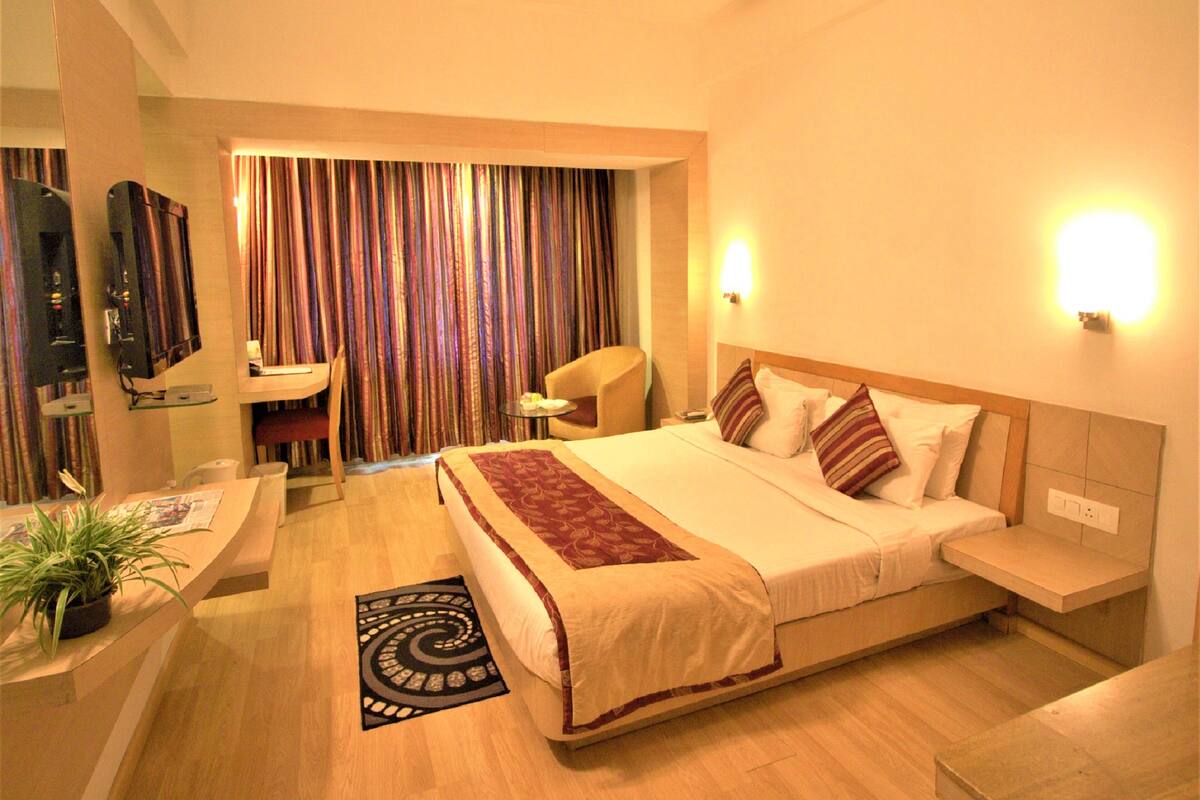 Una habitación de hotel con cama, mesita de noche, silla, televisor y cortinas.