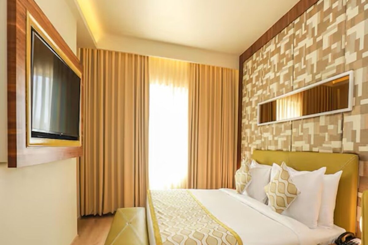 Habitación de hotel con cama, una banca, televisor y cortinas.