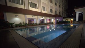 A swimming pool with a tiled deck, surrounded by potted plants and a building with multiple windows and doors. - IRA By Orchid Bhubaneswar (Bhubaneshwar)