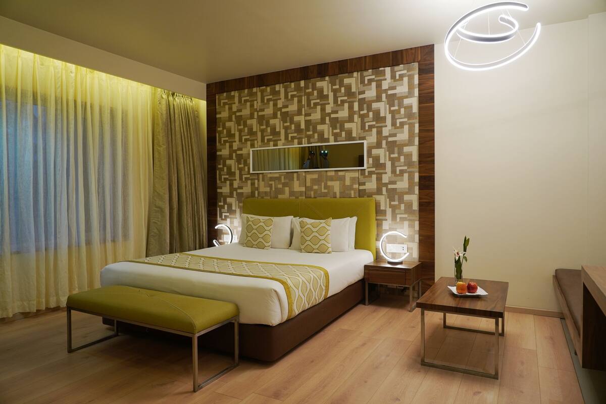 Una habitación de hotel moderna con una cama grande, mesitas de noche, una pequeña mesa con fruta y un espejo.