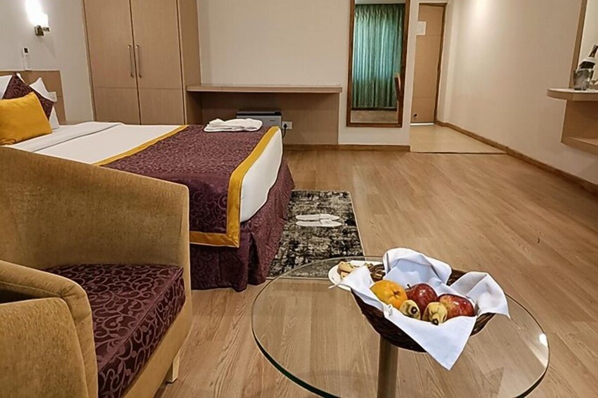 Habitación de hotel con cama, sofá, escritorio, espejo y una mesita con fruta.