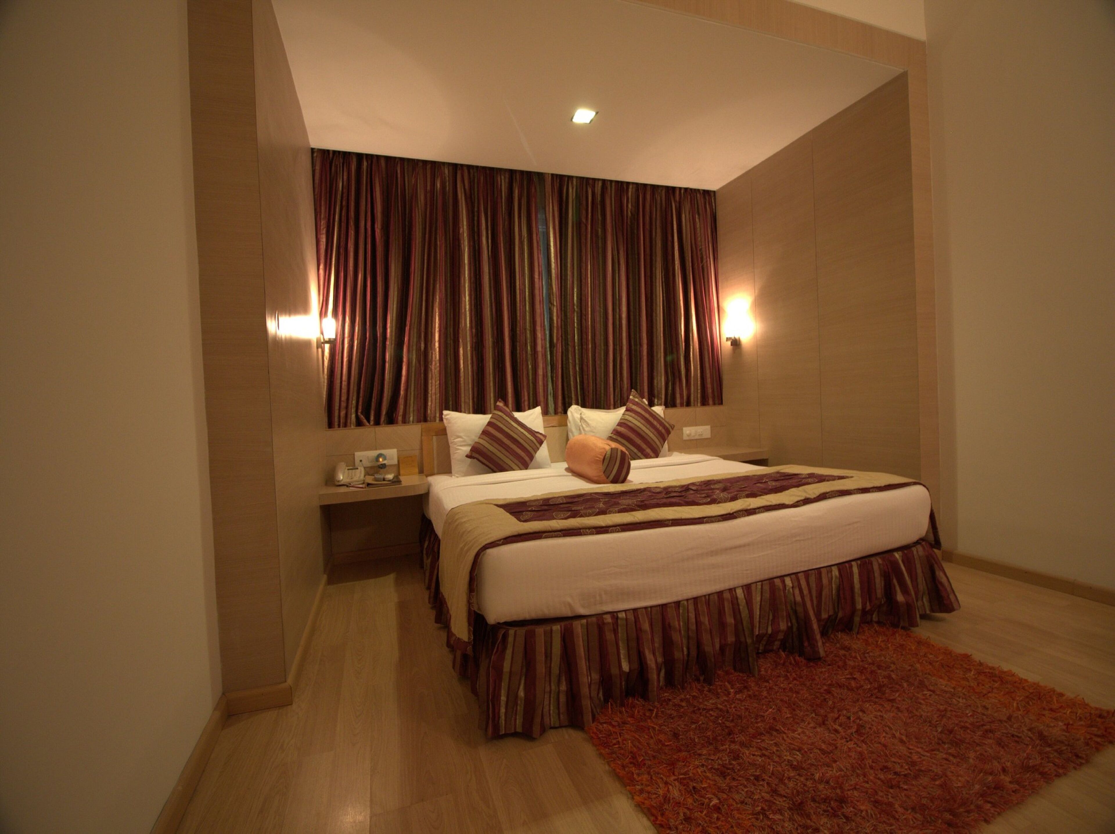 A hotel room with a large bed, a wooden nightstand, a red rug, and a curtain with a striped pattern.