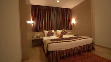 A hotel room with a large bed, a wooden nightstand, a red rug, and a curtain with a striped pattern.