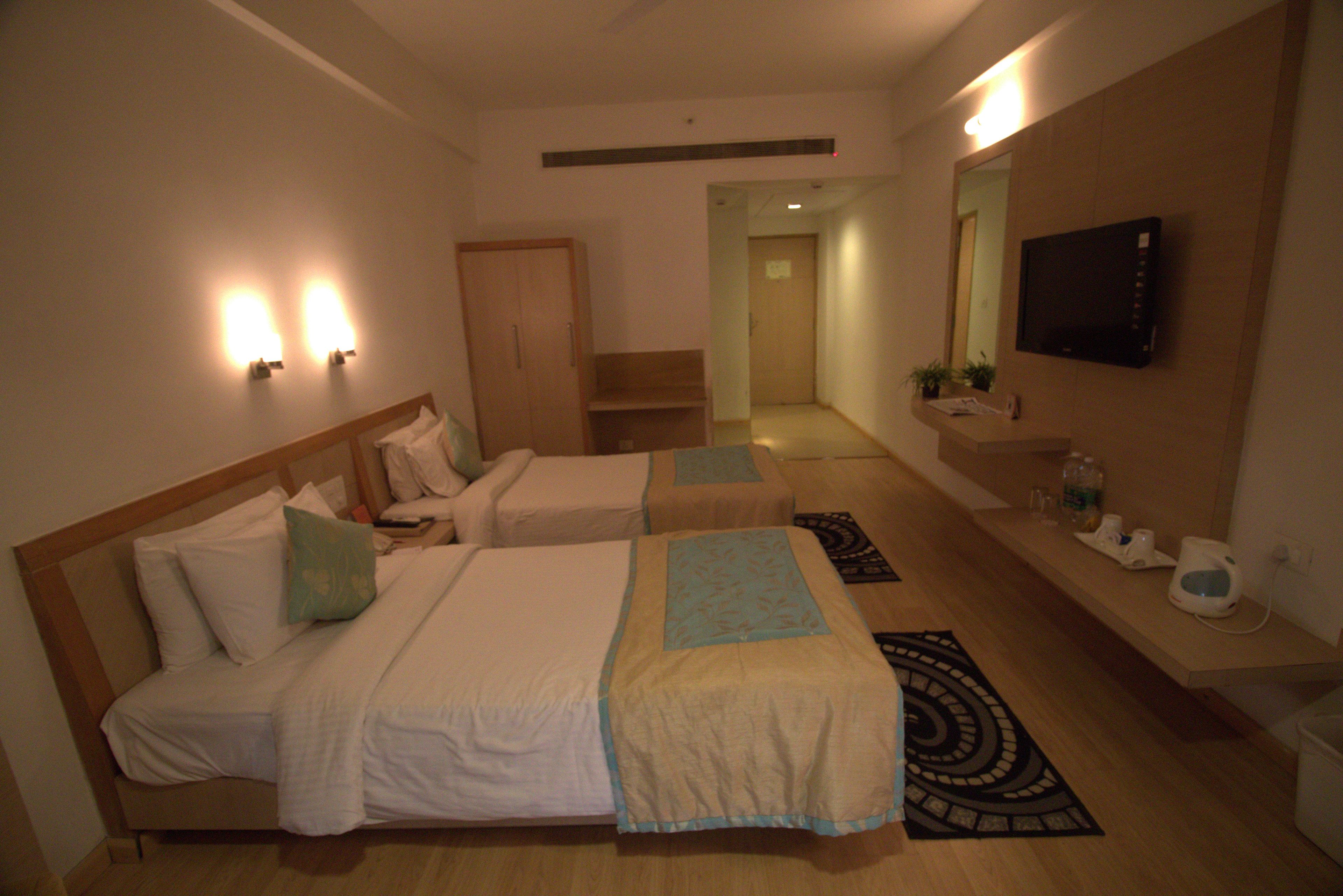 Habitación de hotel con dos camas, un televisor fijado a la pared, un armario de madera y un baño pequeño.