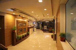 Un vestíbulo de hotel con una recepción, plantas en macetas, un ventanal grande y un techo curvo con iluminación empotrada.