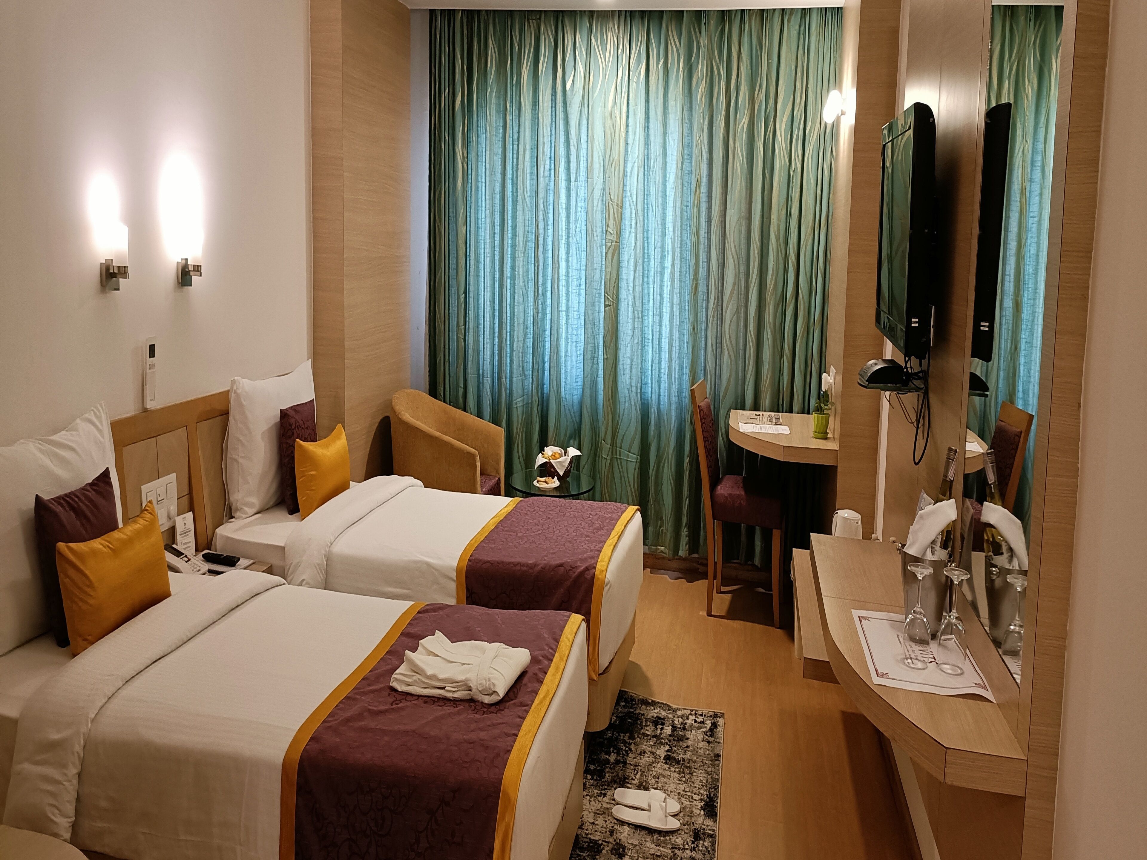 A hotel room with two beds, a desk, a chair, a small table with a vase, and a mirror.