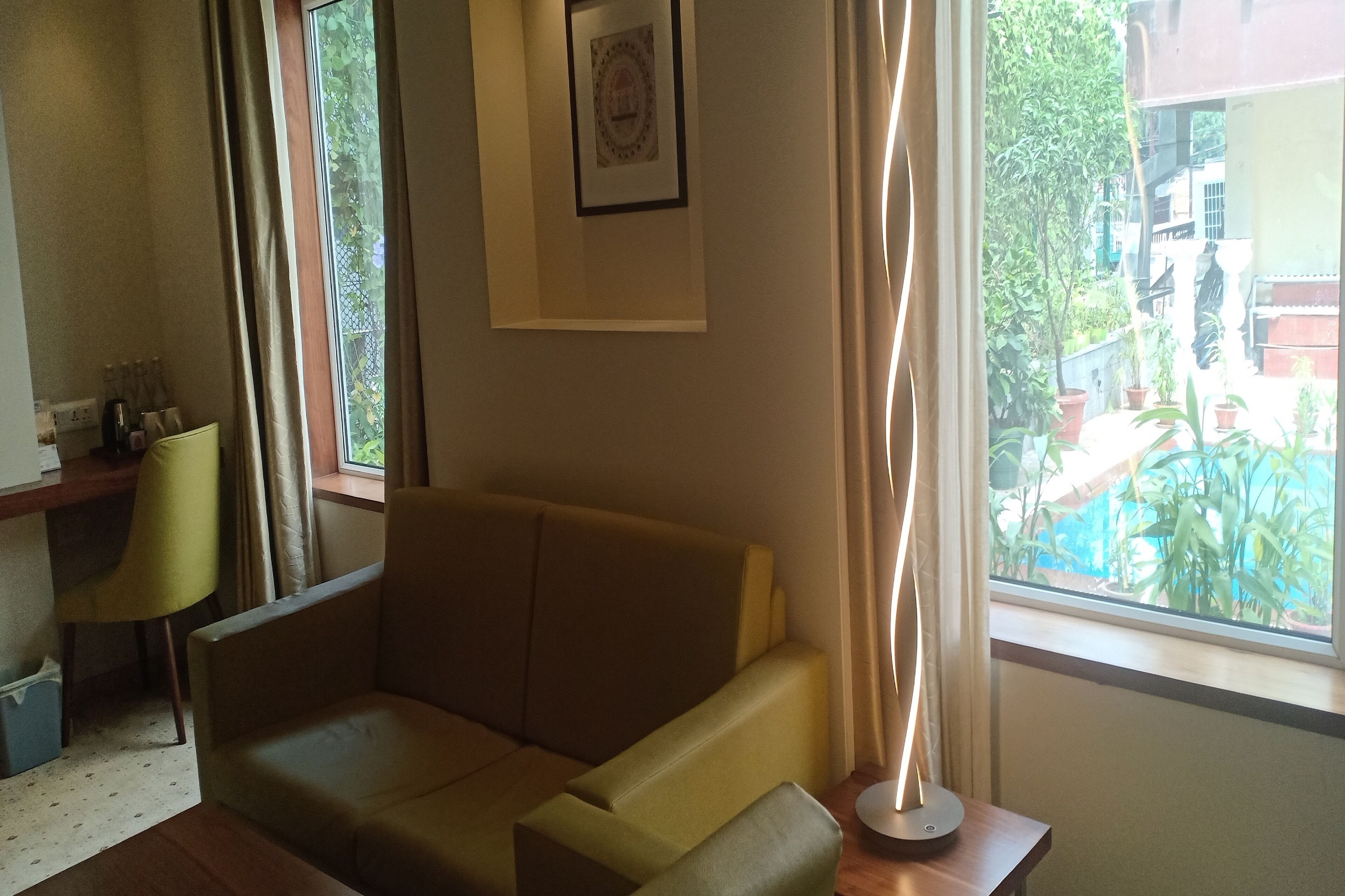 Una sala de estar con un sofá, una mesita, una silla, un cuadro en la pared y una ventana con vistas al exterior.