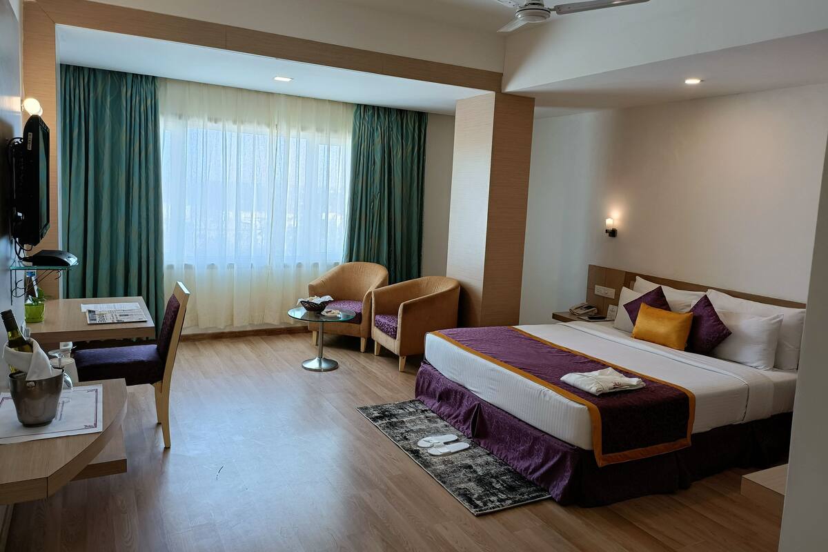 Habitación de hotel con cama, escritorio con silla, una mesita y ventilador de techo.