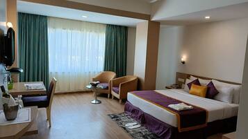 A hotel room with a bed, a desk with a chair, a small table, and a ceiling fan.