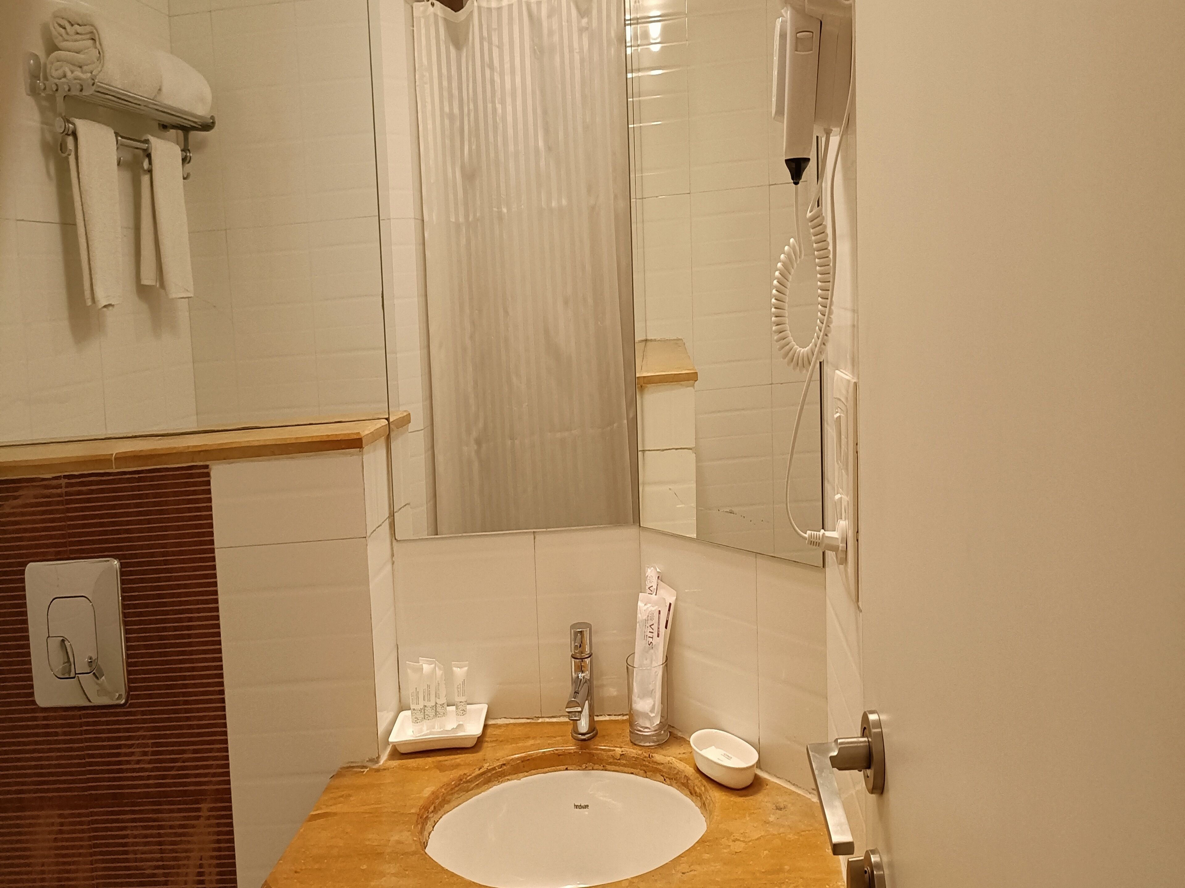 Bagno con mobile contenitore in legno, lavabo bianco, specchio, porta asciugamani, doccia e asciugatore di mani.