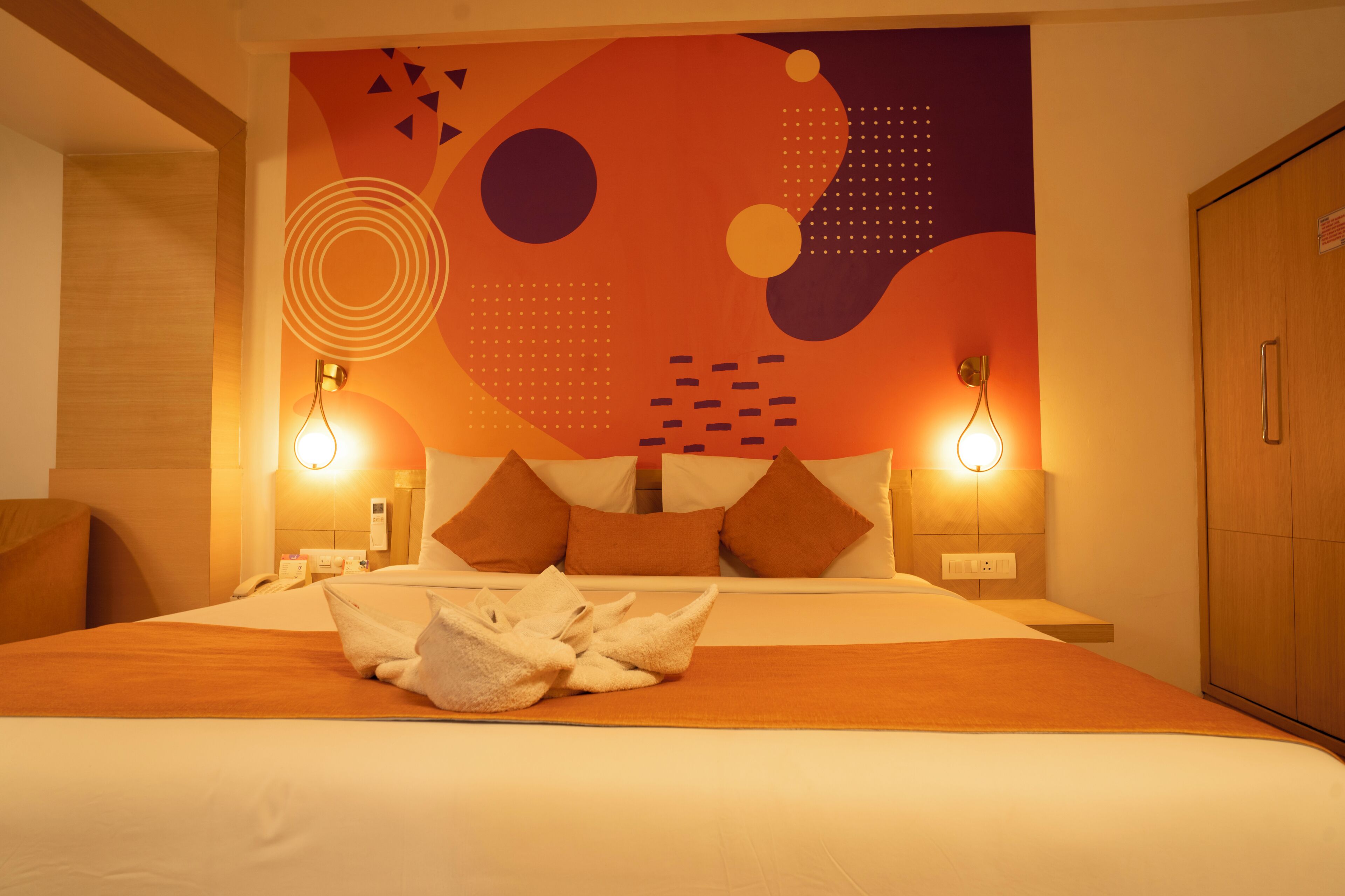 A hotel room with a bed, pillows, a wall art design, and two bedside lamps.