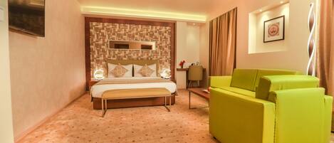 A hotel room with a bed, a green sofa, a desk, and a wall-mounted TV.