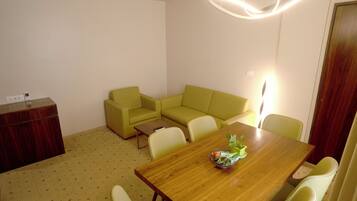 A room with a wooden dining table, a green sofa, and a wooden cabinet.