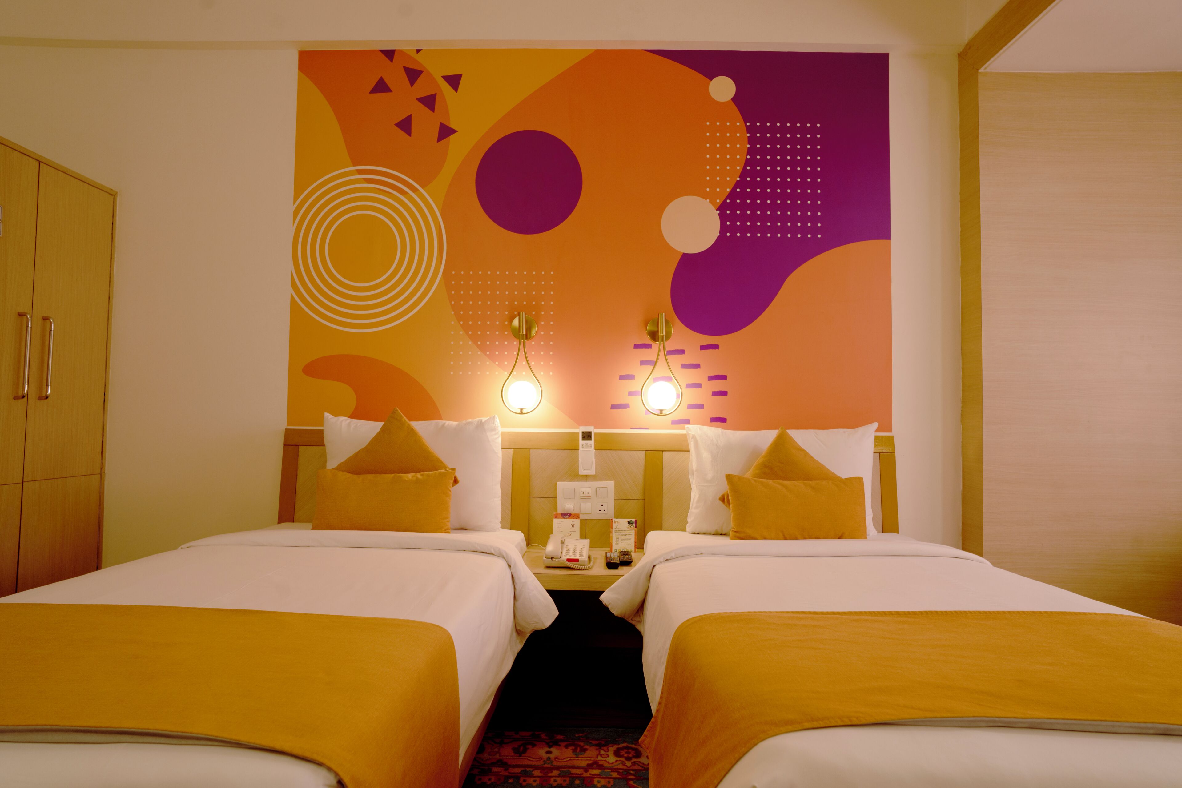 A hotel room with two beds, a large abstract wall mural, and a wooden wardrobe.