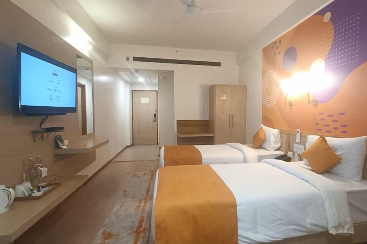 Habitación de hotel con dos camas, un televisor, un escritorio con hervidor y una pared con diseño decorativo.