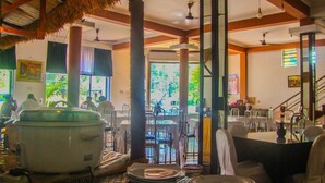 A restaurant with a thatched roof, indoor seating, and a view of the outdoors. - Hotel Mahawasala (Dambulla)