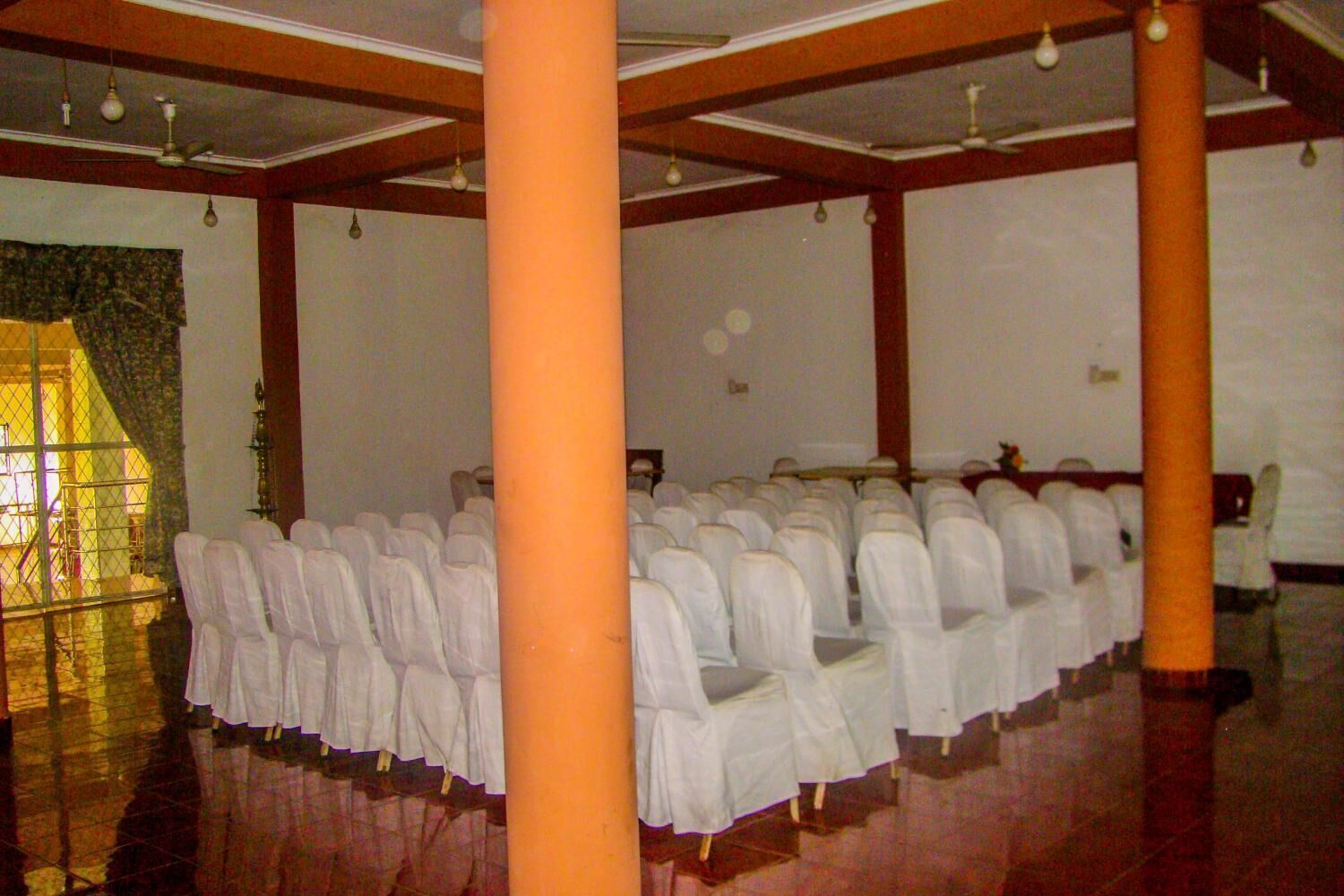 A room with rows of white chairs, wooden pillars, and a tiled floor.
