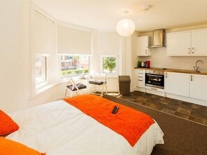A compact hotel room with a bed, a small kitchenette, and a window offering a view of the outdoors.