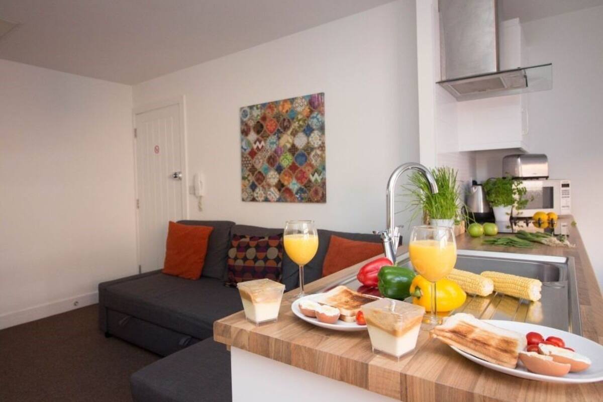 A modern kitchen with a dining area, a sofa, and a colorful artwork on the wall.