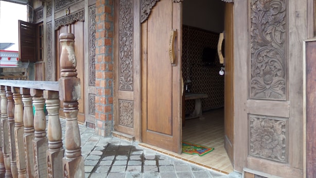 A wooden entrance with intricate carvings, a brick column, and a tiled floor. - Pondok Wisata Adas (Ngadisari)