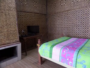 A room with a bed, a television on a wooden table, and patterned walls. - Pondok Wisata Adas (Ngadisari)