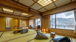 A traditional Japanese room with tatami flooring, a low table, a cushion, and a view of a snowy landscape through large windows. - Aonobi Yuyu (Biei)