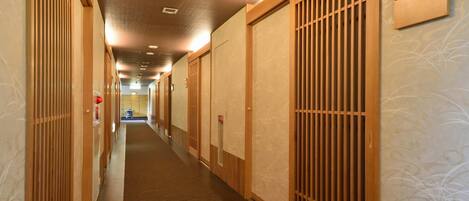 A hotel hallway with traditional wooden sliding doors, a carpeted floor, and a ceiling with recessed lighting.