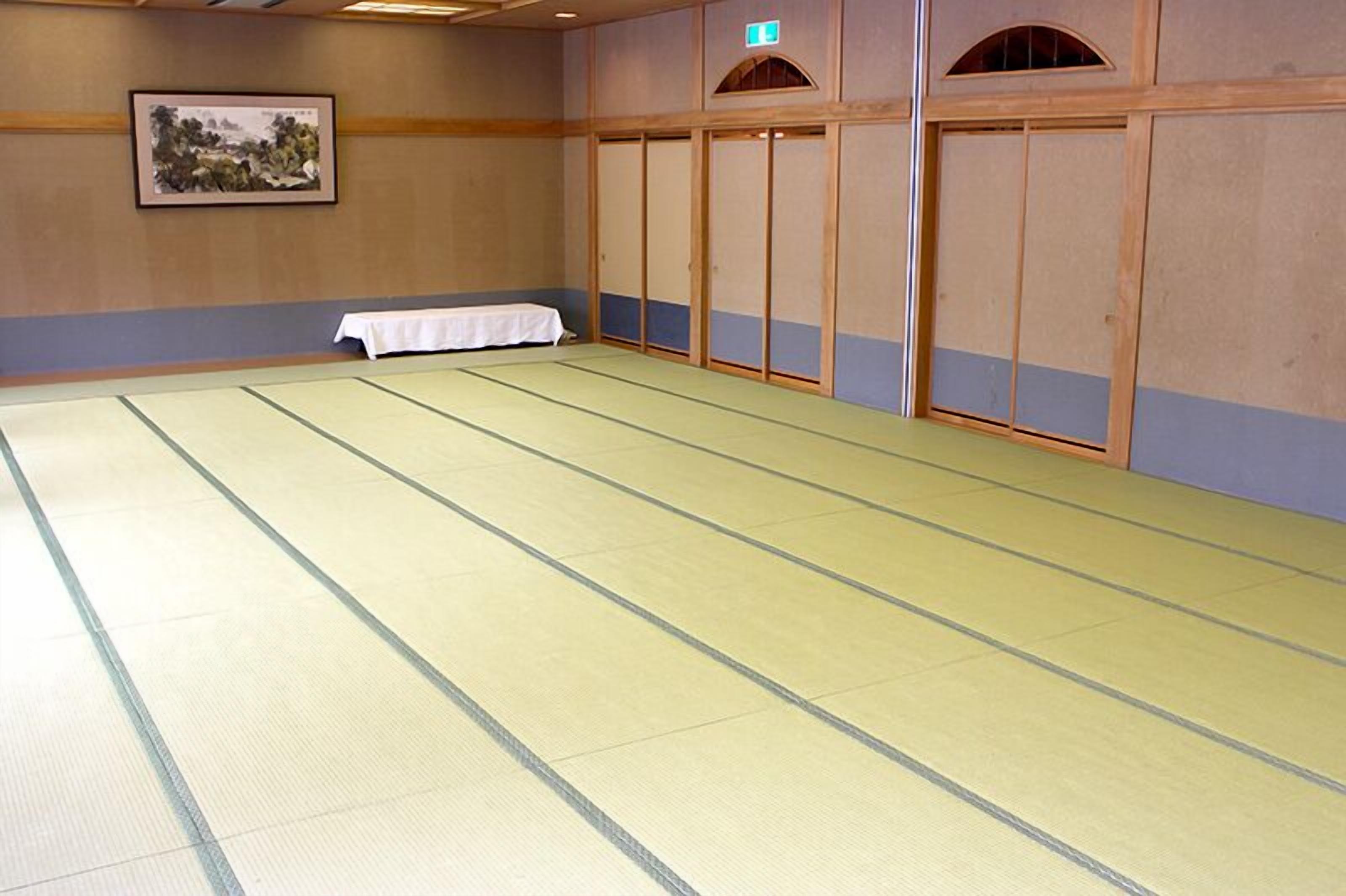 A tatami mat room with a table, wooden sliding doors, and a framed picture on the wall.