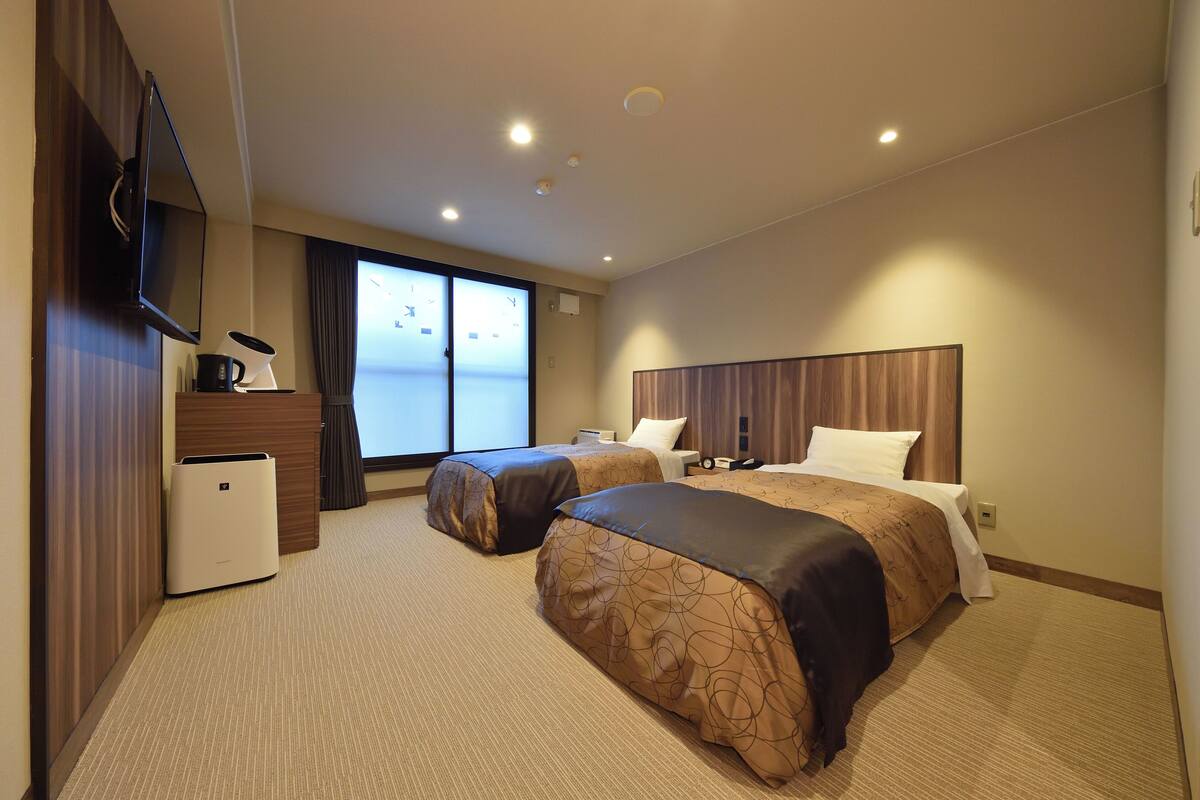 Ein Hotelzimmer mit zwei Betten, einem Flachbildfernseher, einer Kaffeemaschine und Blick ins Freie.