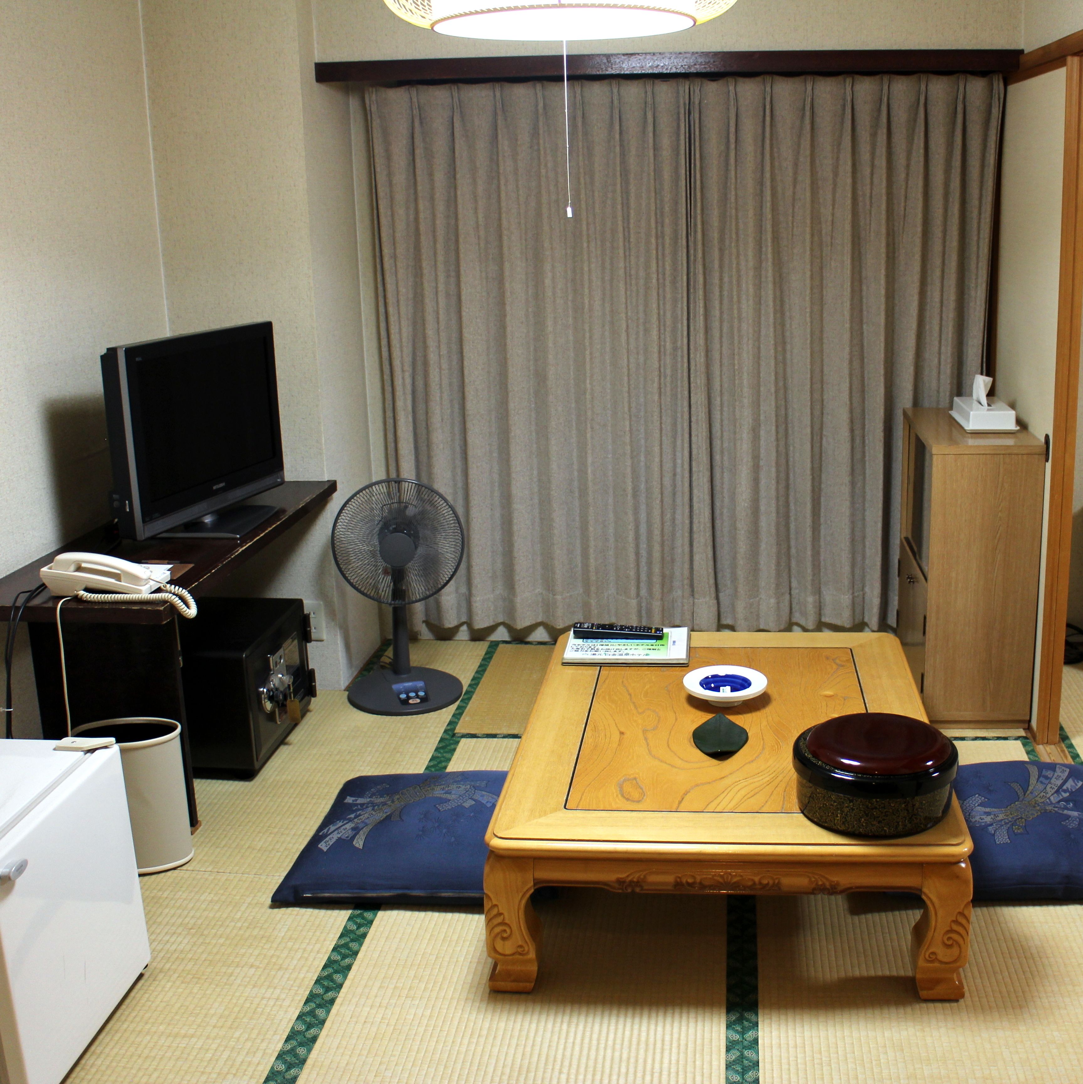 A hotel room with a television, a fan, a small table with a bowl and a remote control, and a wooden cabinet.
