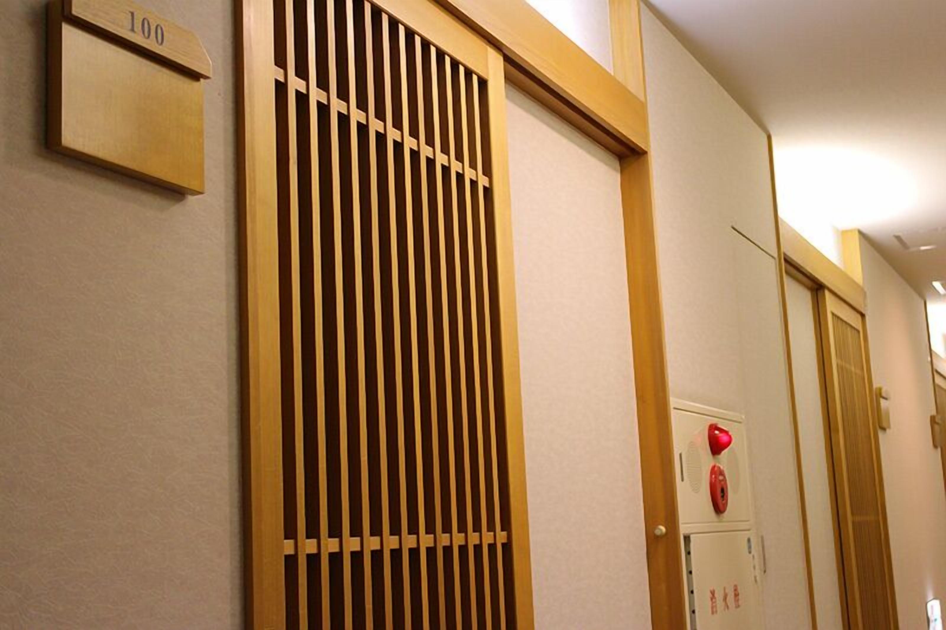 Interior de un hotel con un panel divisor de listones de madera, un detector de incendios y una puerta con placa de número.
