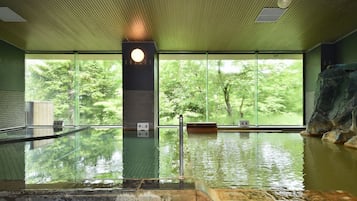 Une piscine intérieure avec des parois en verre transparent, un mur en pierre et un plafond en bois.