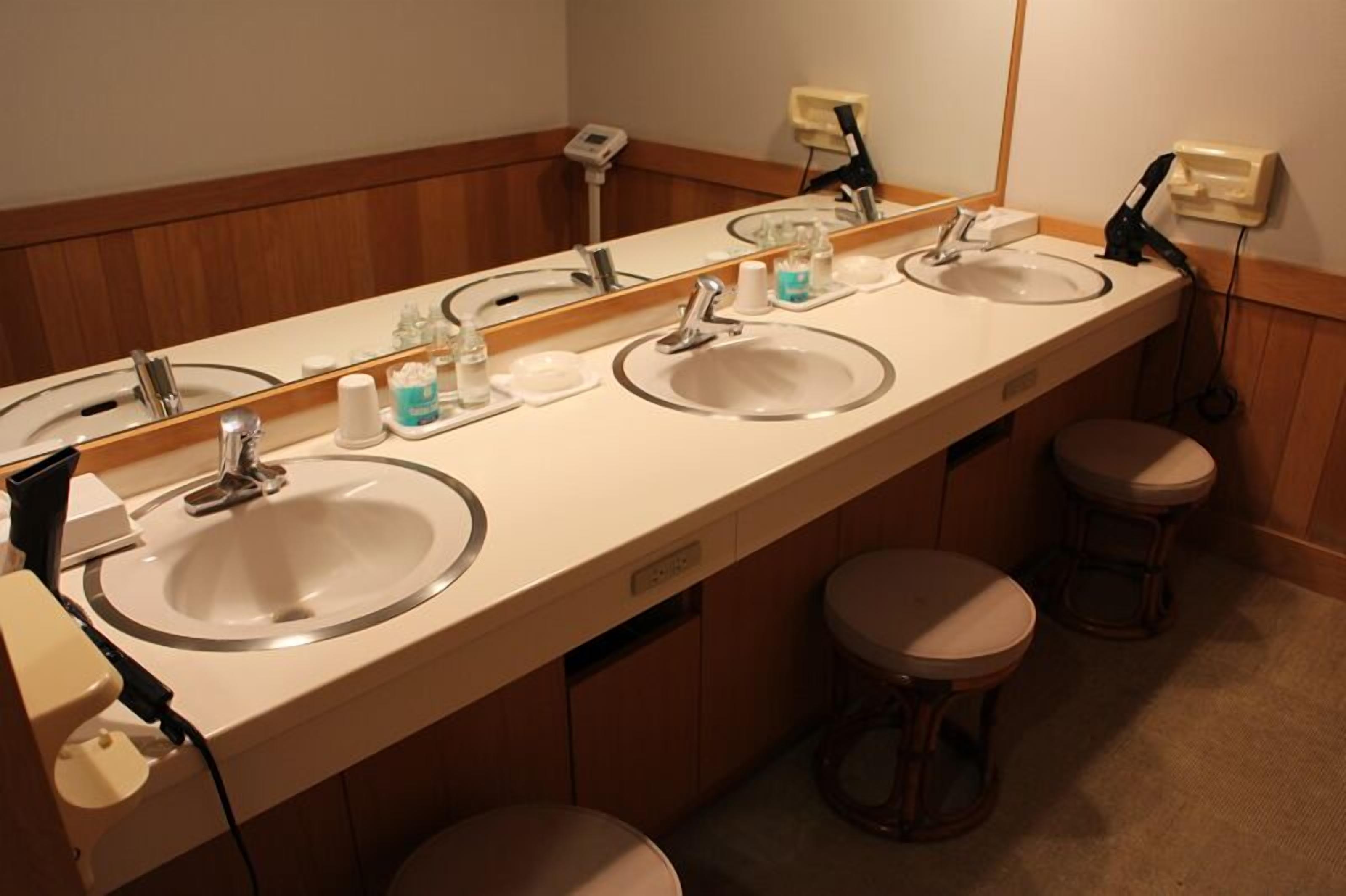 A hotel bathroom with three sinks, a large mirror, and two stools.