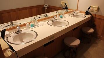 A hotel bathroom with three sinks, a large mirror, and two stools.