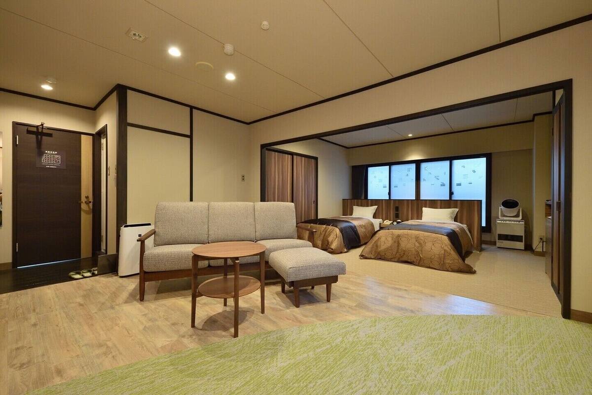 Ein Hotelzimmer mit einer Couch, einem kleinen Tisch, zwei Betten, einem Fenster und einer Tür.