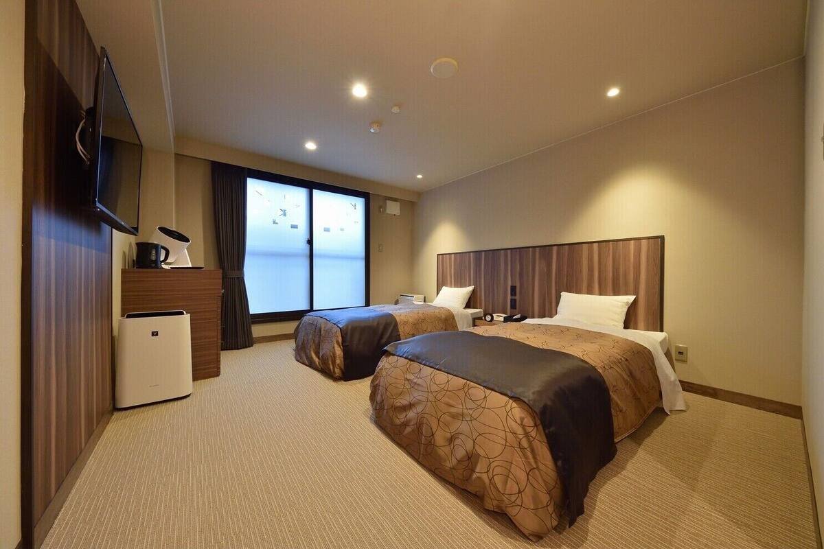 Ein Hotelzimmer mit zwei Betten, einem Schreibtisch, einem Flachbildfernseher und einem großen Fenster.
