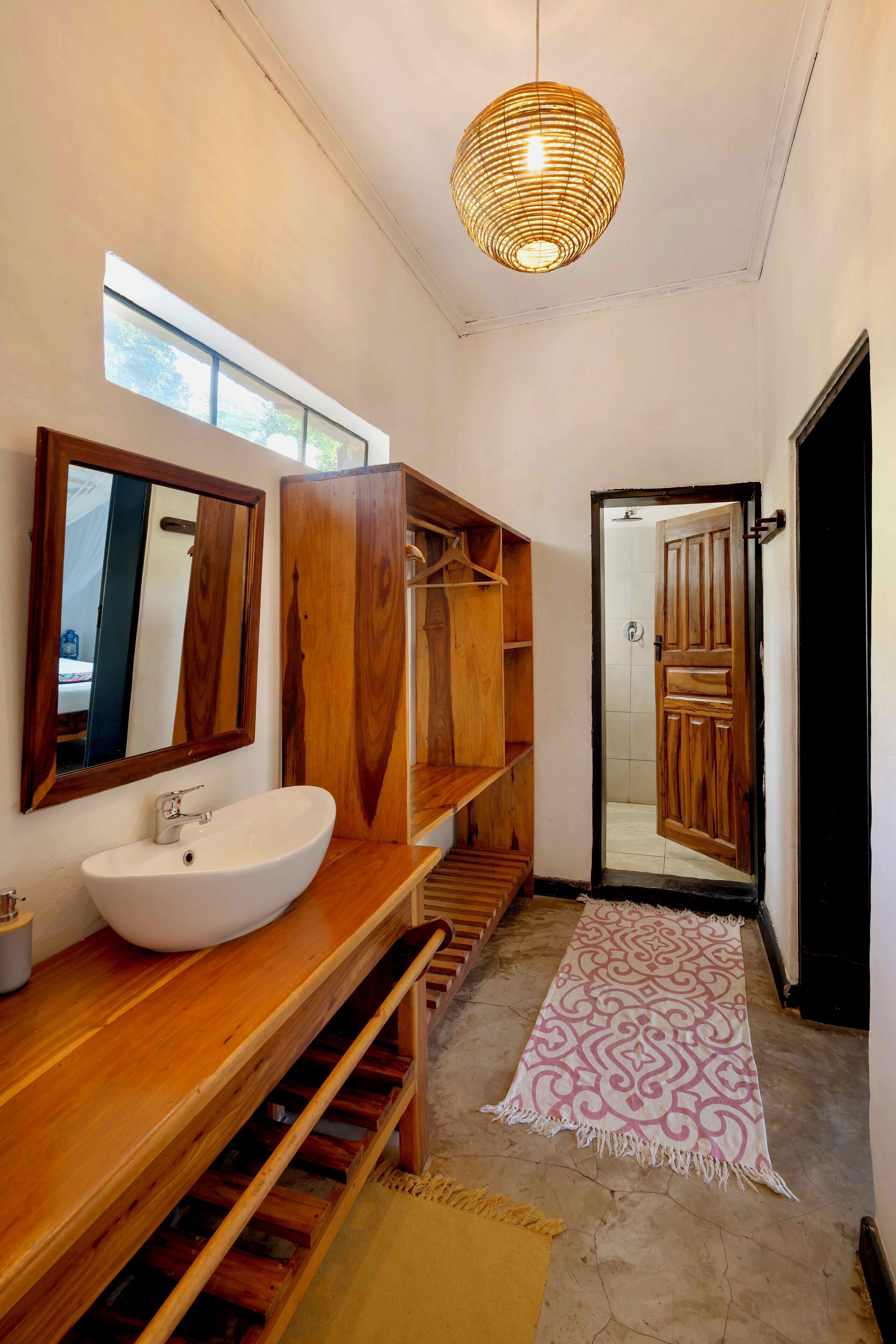 A modern bathroom with a wooden vanity, a large mirror, a white sink, and a woven light fixture.