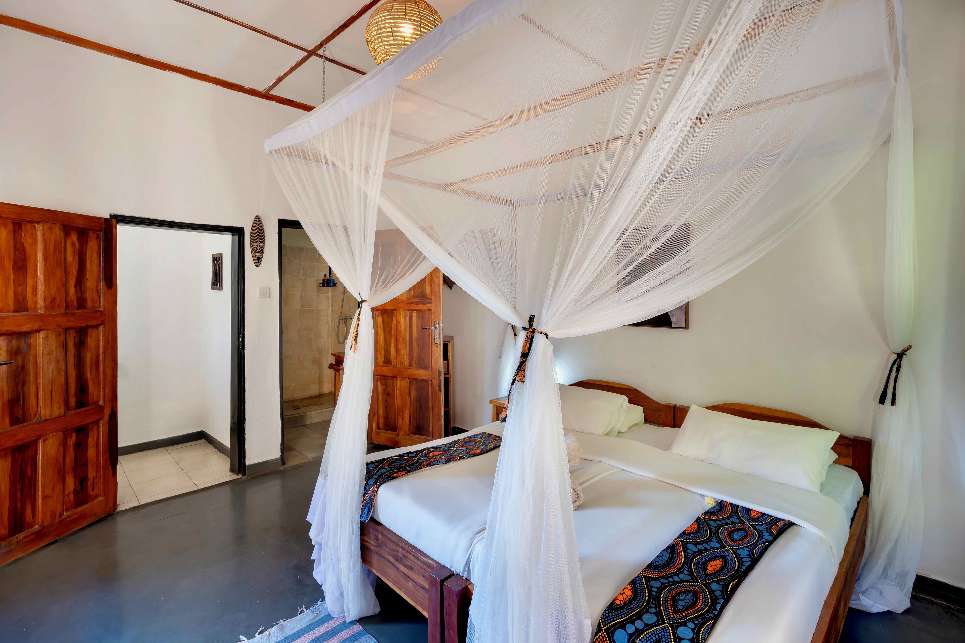 Une chambre avec un lit sous un dais, des portes en bois et un aménagement simple et épuré.