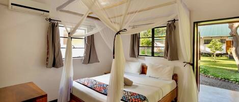 A bedroom with a canopy bed, a wooden headboard, and a view of the garden.