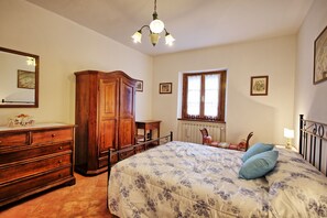 A bedroom with a bed, wooden wardrobe, dresser, and a window with curtains. - Villa Portole Due (Cortona)
