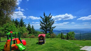 A playground with a slide and climbing structure, surrounded by a grassy area and a view of mountains. - Villa Portole Due (Cortona)