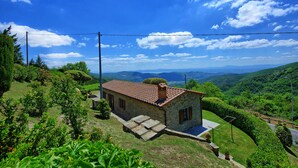 A stone house with a red-tiled roof, surrounded by lush greenery and hills in the background. - Villa Portole Due (Cortona)