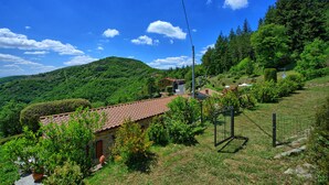 A rural house with a red-tiled roof, surrounded by lush greenery and a clear blue sky. - Villa Portole Due (Cortona)