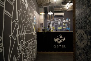 Un área de recepción con un mostrador negro que muestra la palabra "OSTEL" y una pared con dibujos lineales en blanco.