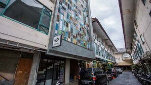 Un edificio de varios pisos con diversas tiendas en la planta baja, un letrero que dice "OSTEL" y varios vehículos estacionados.