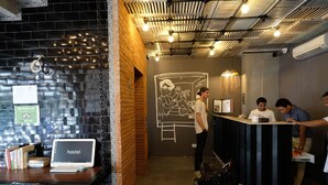 Una zona de recepción con una laptop mostrando 'hostel', una pared de ladrillo y un mural.