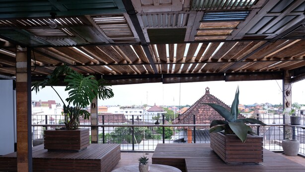 Un área de estar al aire libre techada con bancos de madera y macetas, con vistas a un paisaje urbano.
