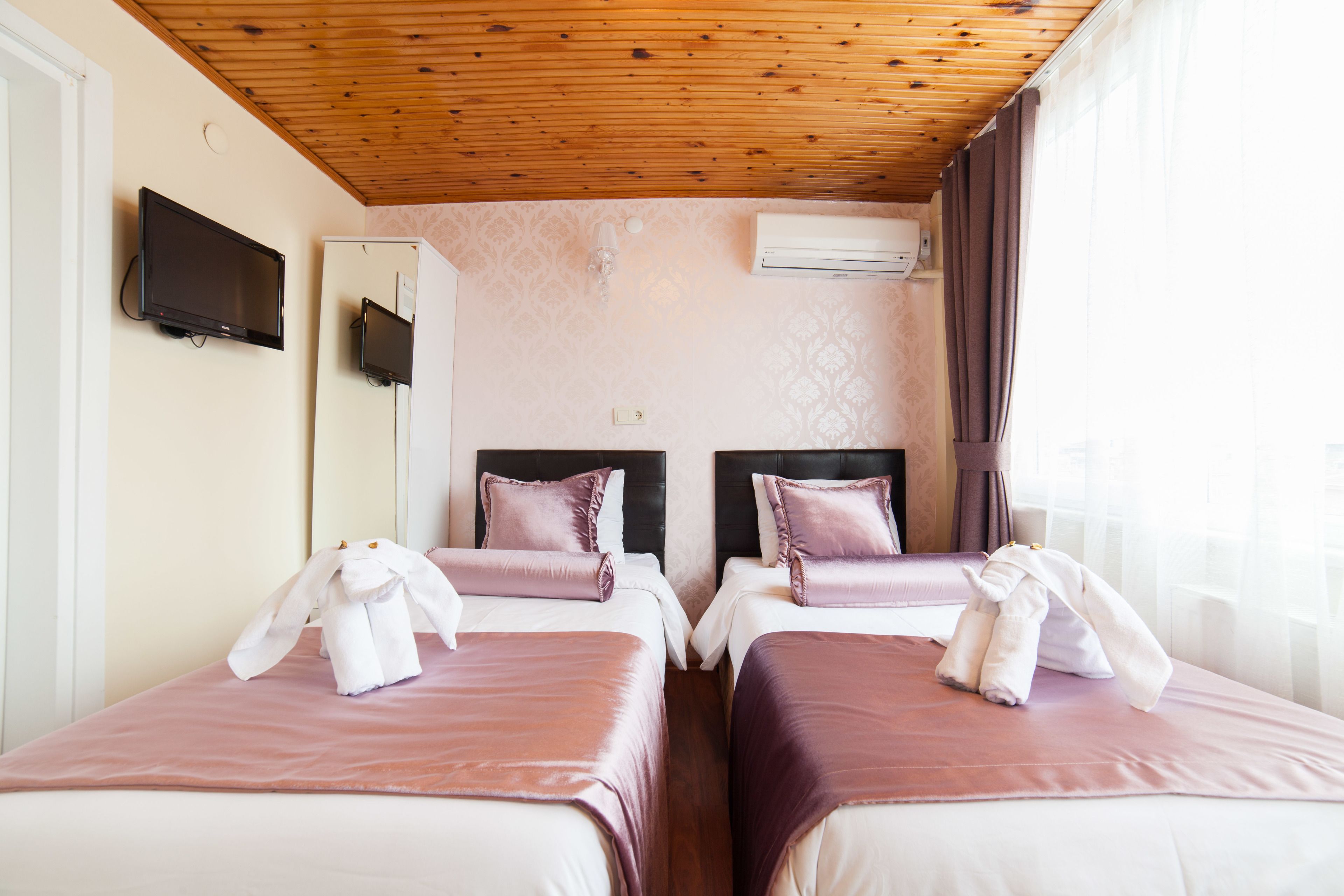 A hotel room with two beds, wooden ceiling, air conditioning unit, and a flat-screen TV.