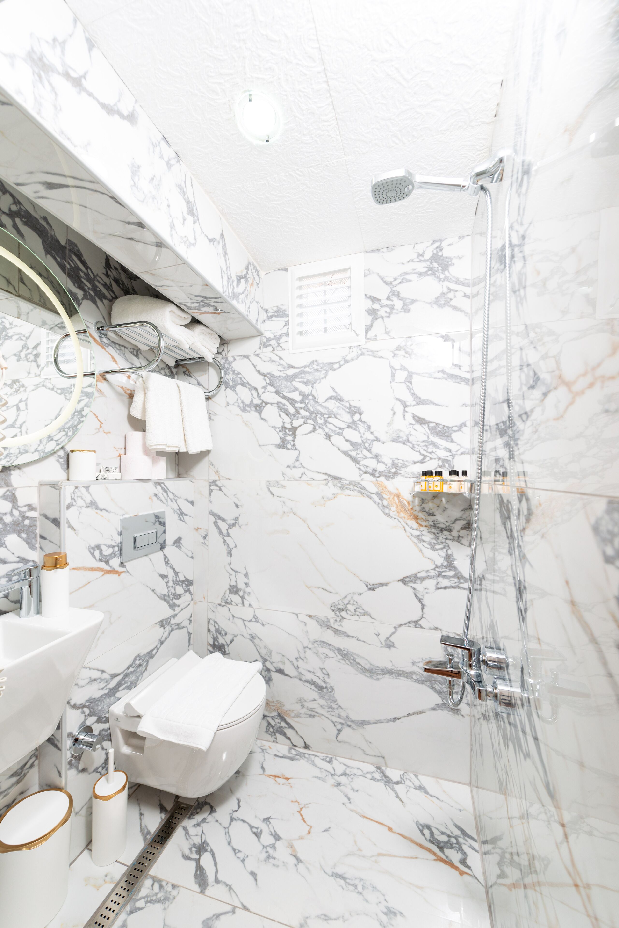 A bathroom with a marble floor, a toilet, a sink, and a shower.