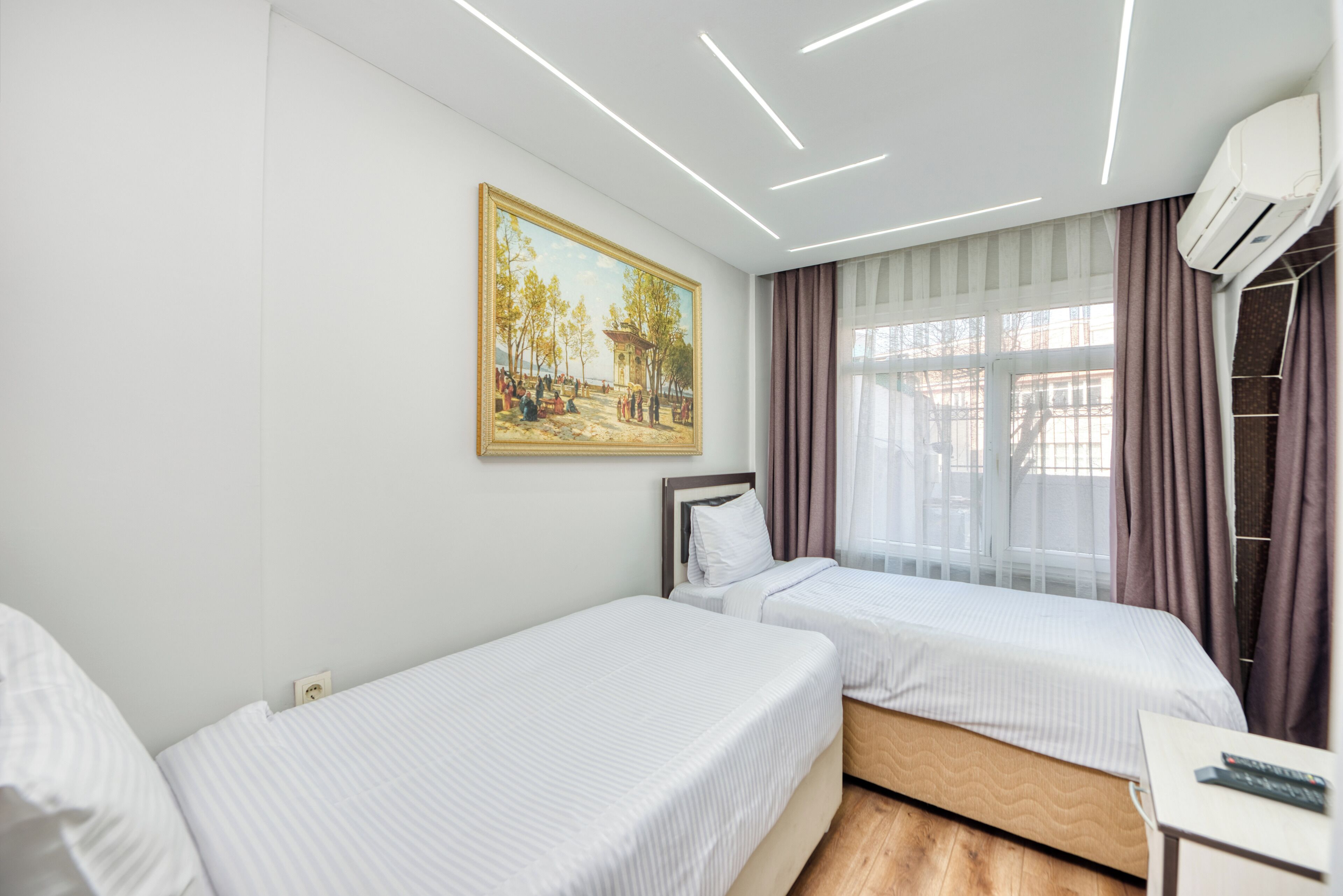 Hotelkamer met twee bedden, een schilderij aan de muur, een raam met gordijnen en een airconditioning.